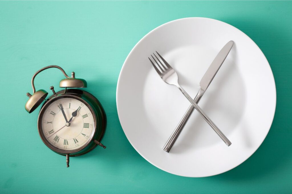 時計と交差したフォークとナイフ、断食や食事時間制限を示すイメージ。
