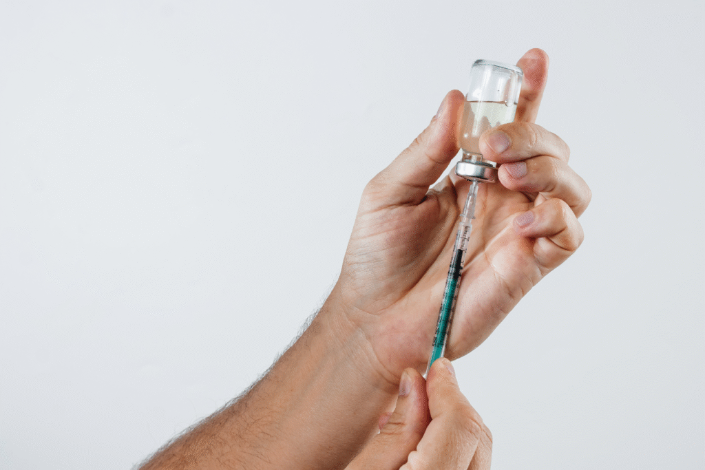 薬液の入ったバイアルから注射器に薬剤を吸い上げる手元。成長ホルモン投与や医療行為の象徴的イメージ。