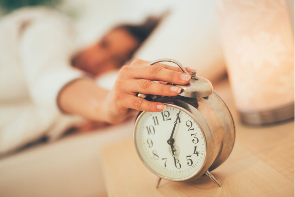 ベッドで目覚まし時計を止めようとする寝起きの女性の手