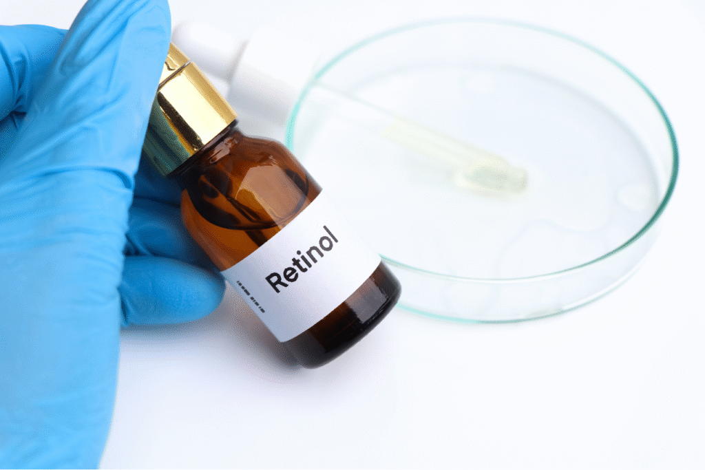 青い手袋をした手が持つ「Retinol」とラベルされたガラス瓶。後方にはスポイトと透明な液体が入ったシャーレがある