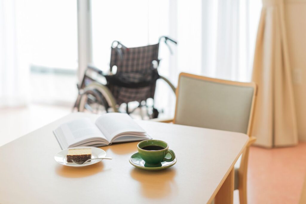 車椅子が置かれた明るい部屋で、テーブルに開いた本とコーヒーとケーキ