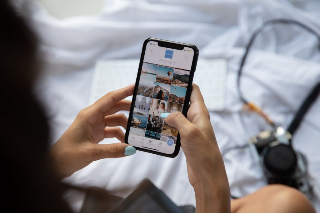 スマートフォンを操作する女性の手元。画面には旅行や風景写真が並ぶSNSのプロフィールページが表示されている。