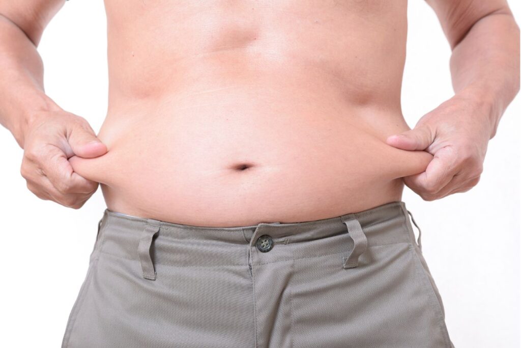 上半身裸の中年男性がお腹の脂肪を指でつまんでいる様子