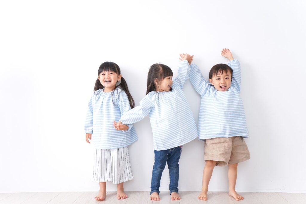 おそろいのスモック姿で笑顔を見せる幼い子ども3人