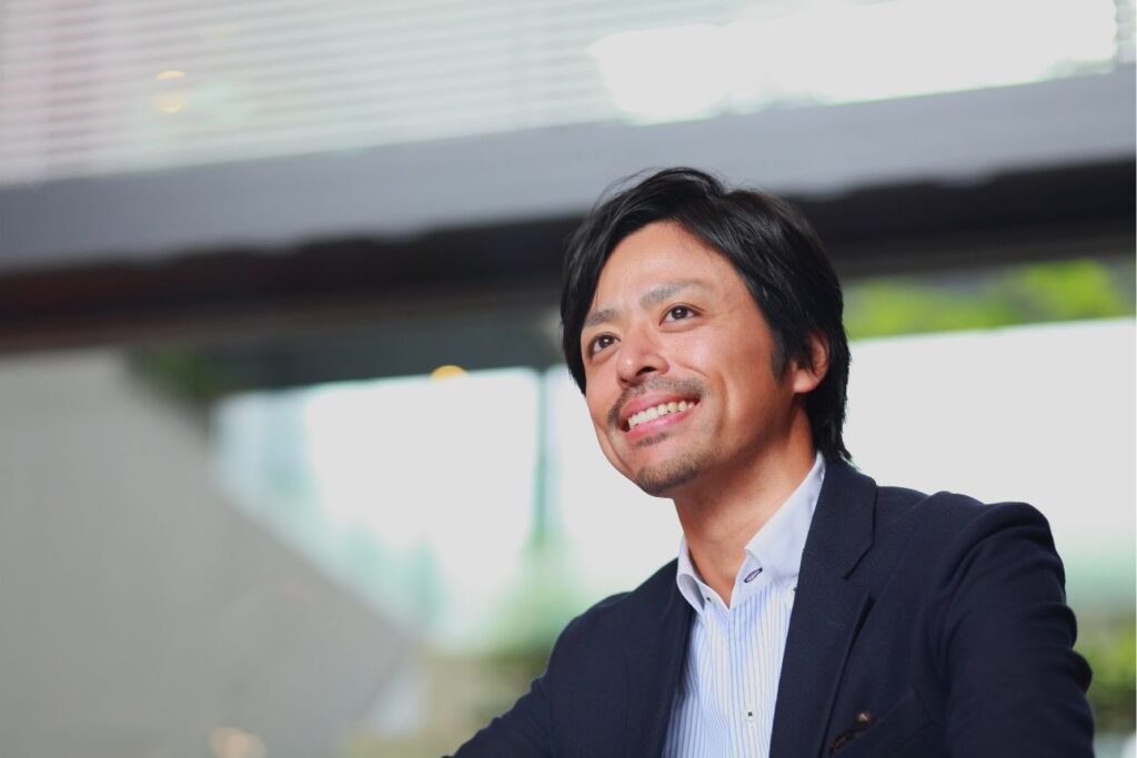 屋内で笑顔を見せるスーツ姿の若い男性。