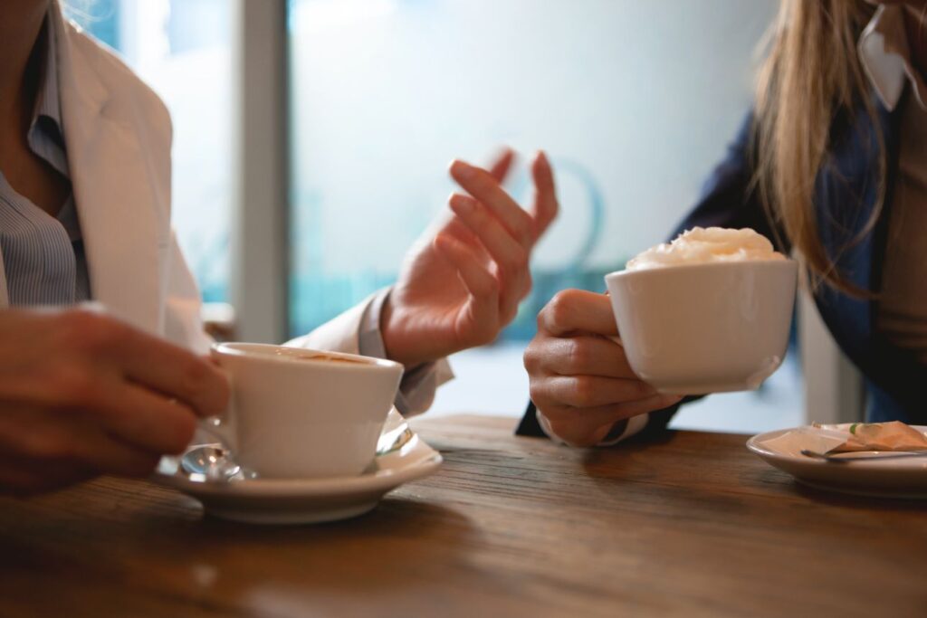 カフェでカップを持ちながら会話する二人のビジネスパーソンの手元