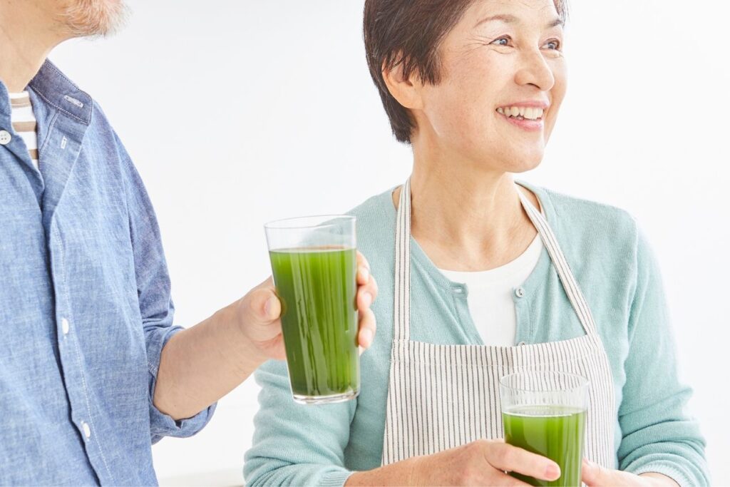 笑顔で青汁のような緑色ドリンクを手にするシニア夫婦の上半身