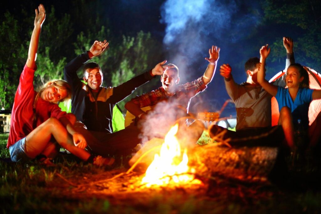 夜のキャンプファイヤーを囲んで手を挙げて盛り上がる若者グループ