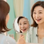 鏡に映る自分を見て笑顔になる50代女性。若々しい肌と嬉しそうな表情が特徴。