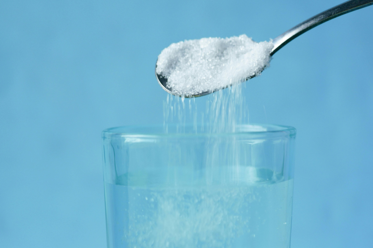 スプーンからグラスの水に砂糖を入れている様子