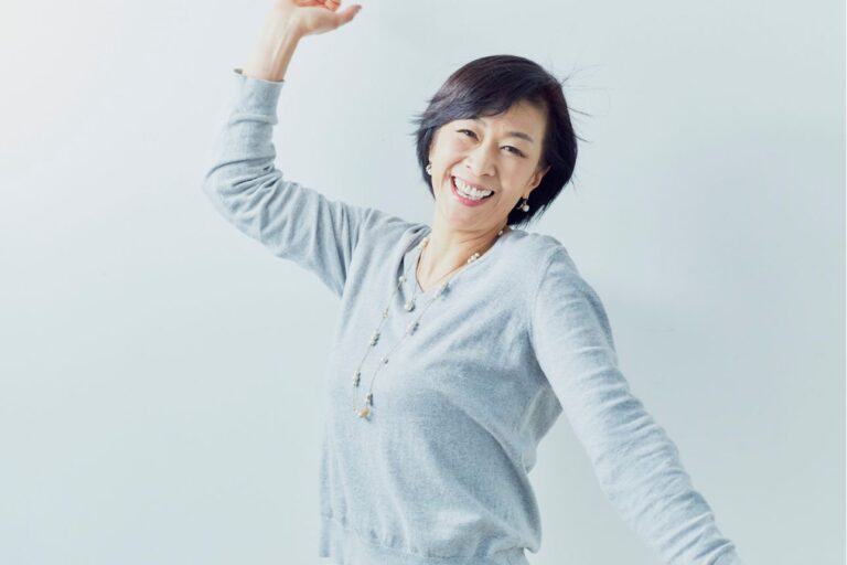 笑顔で腕を上げてポーズを取る中年女性。