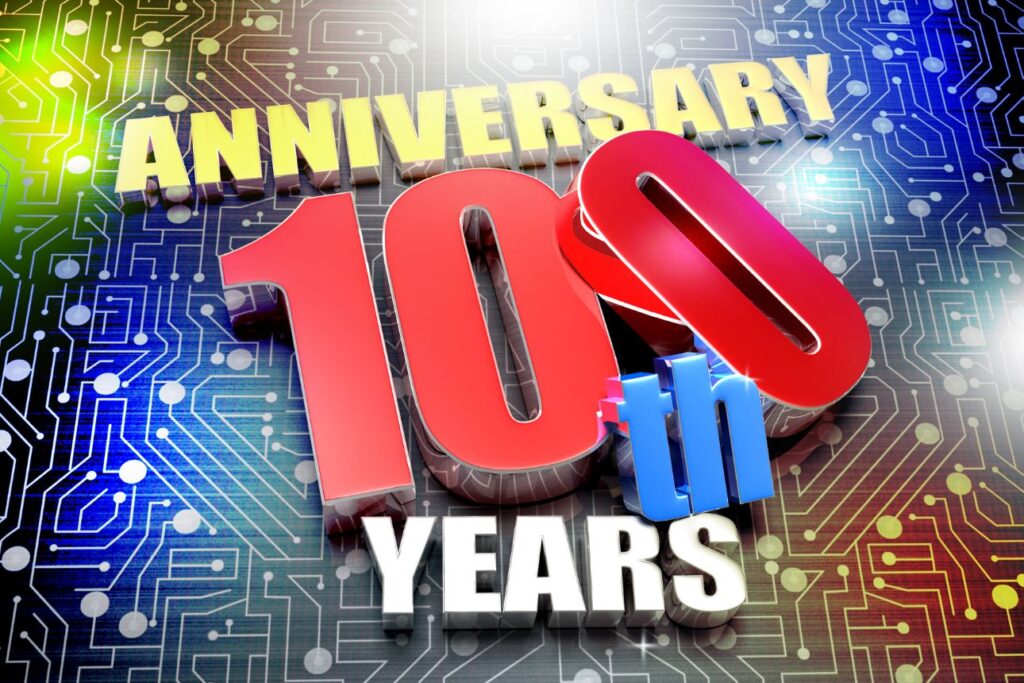 「100周年」を祝うカラフルな3Dロゴとデジタル回路背景のイメージ。