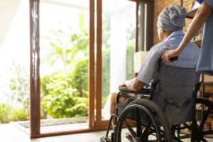 車椅子に座った人物が介助者に押されながら庭を眺めている後ろ姿。
