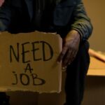 段ボールに「NEED A JOB」と書かれたサインを持つ人物の手元