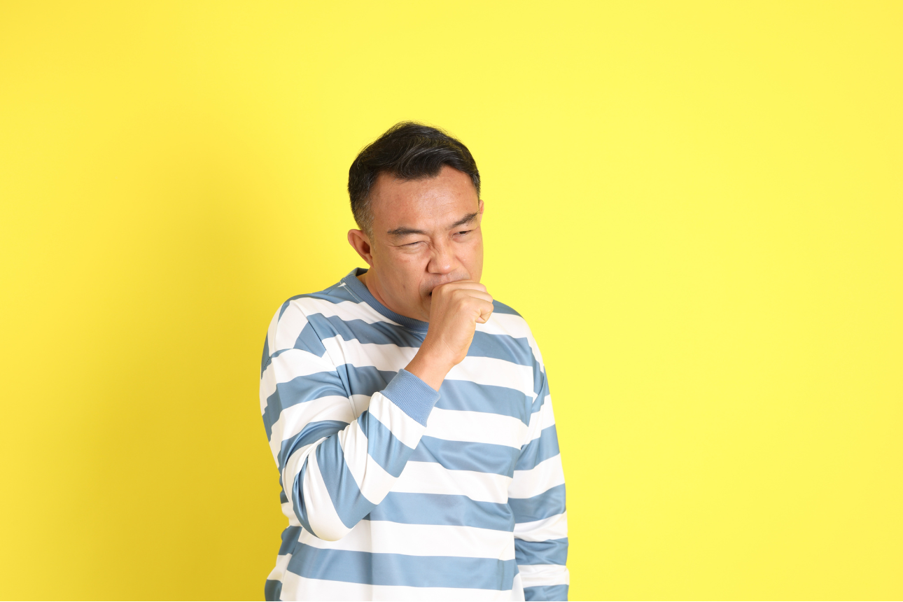 黄色の背景の前で咳き込む男性。疲労や体調不良をイメージさせるシーン