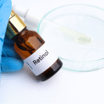 青い手袋をした手が持つ「Retinol」とラベルされたガラス瓶。後方にはスポイトと透明な液体が入ったシャーレがある