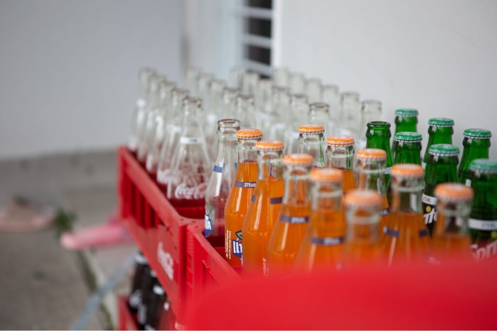 空き瓶と一部未開封の炭酸飲料ボトルが赤いケースに並べられている様子。FantaやSprite、Coca-Colaの瓶が見える。