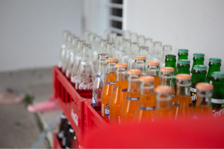 空き瓶と一部未開封の炭酸飲料ボトルが赤いケースに並べられている様子。FantaやSprite、Coca-Colaの瓶が見える。