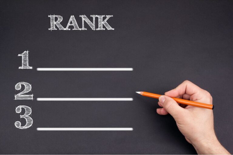 黒板に書かれたランキング表（1位、2位、3位）に、オレンジの鉛筆を持った手が書き込もうとしている様子