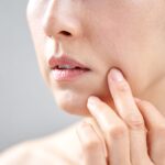 頬のたるみや肌の状態を指で確認する女性。スキンケアや肌老化に関するイメージ