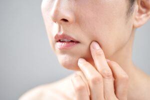 頬のたるみや肌の状態を指で確認する女性。スキンケアや肌老化に関するイメージ