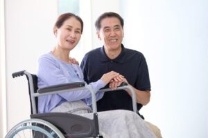 笑顔で寄り添う高齢の夫婦、妻は車椅子に座っている