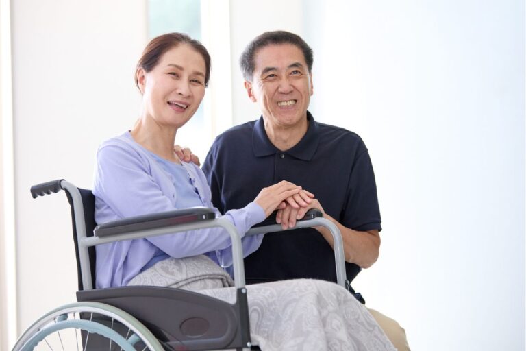 笑顔で寄り添う高齢の夫婦、妻は車椅子に座っている